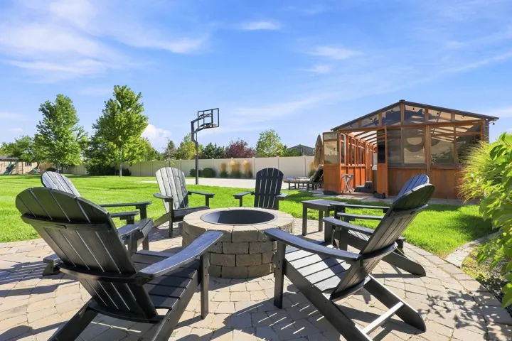 Paved patio with a stone fire pit, extensive lawn, and a wood-frame structure with translucent paneling