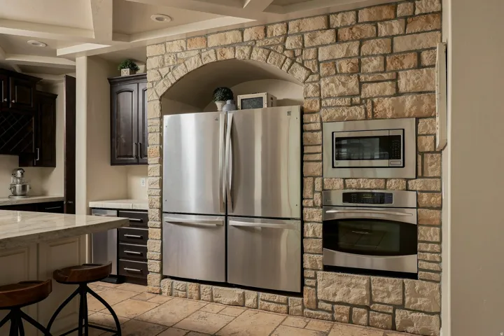 Stone accent wall with an arched alcove, integrated stainless steel appliances, and wood-finish cabinetry