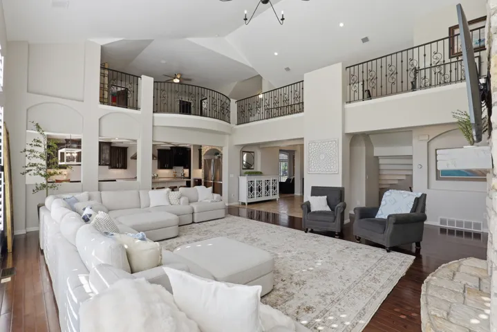 Expansive living area featuring vaulted ceilings, wood-finish flooring, a stone-clad fireplace, and wrought iron balcony railings