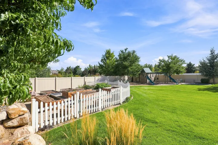 Expansive green lawn, white picket fence, raised garden beds, mature trees, and a privacy fence