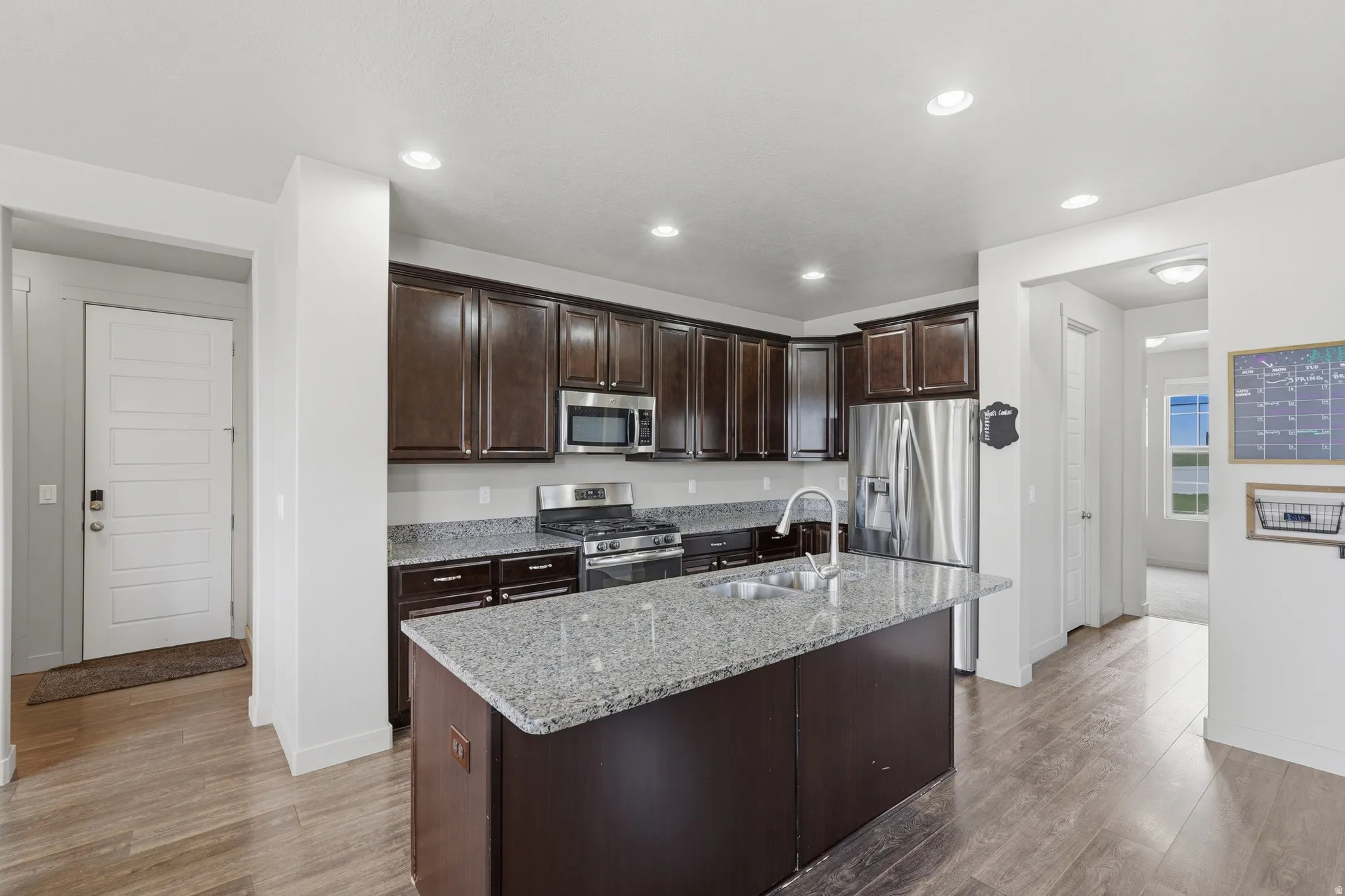 Kitchen featuring dark wood cabinetry, light granite countertops, stainless steel appliances, and a central island with an undermount sink