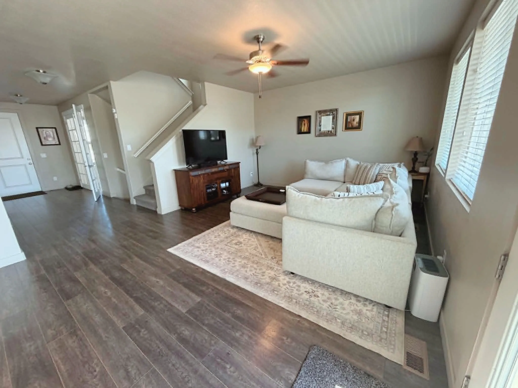 Open-concept living space featuring wood-finish flooring, a contemporary ceiling fan, and staircase with carpeted treads