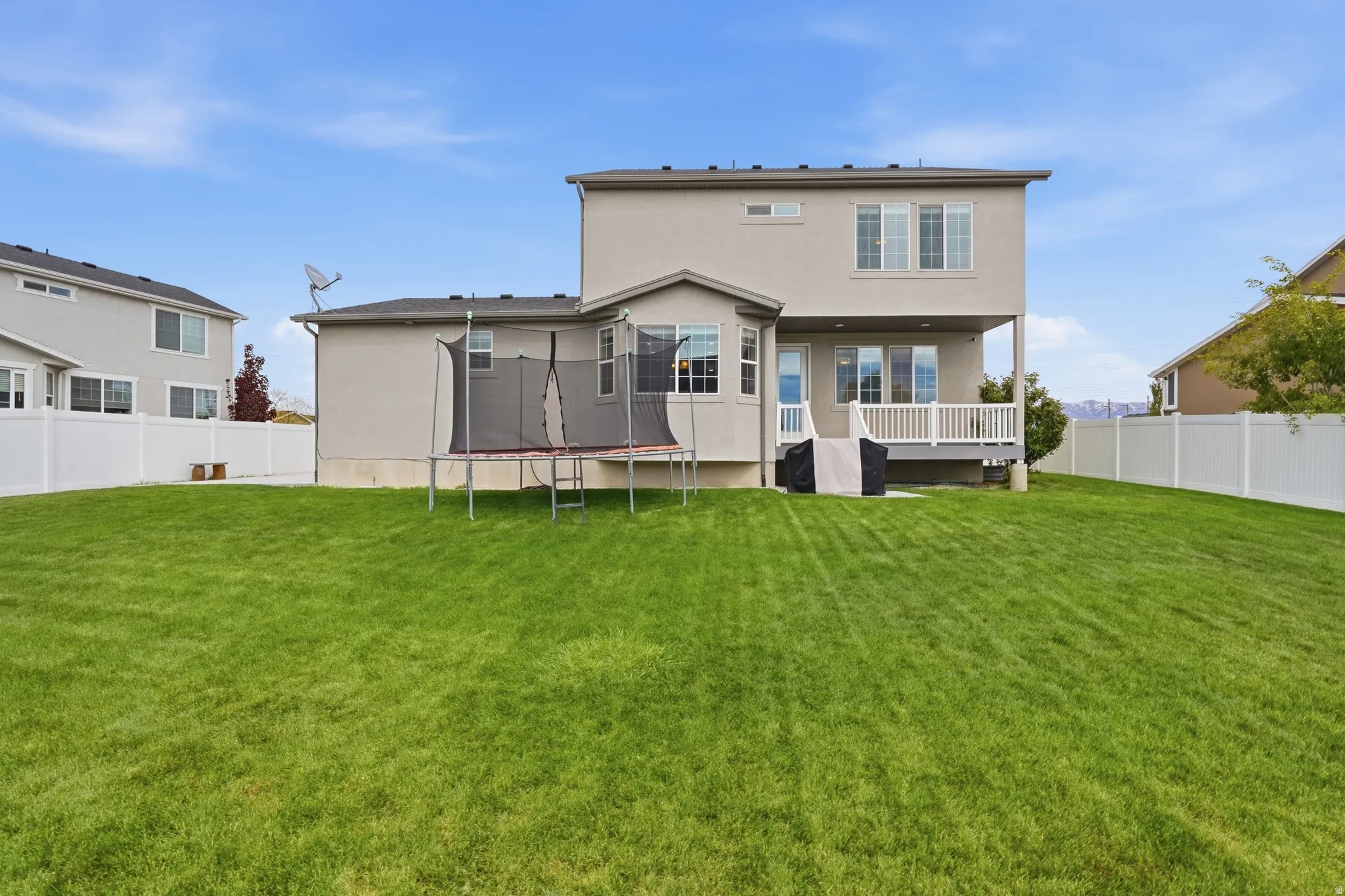 Rear view of house with a trampoline, a fenced backyard, stucco siding, and a deck