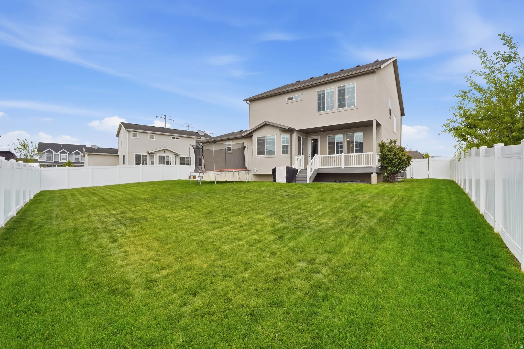 Back of property featuring a deck, a fenced backyard, a trampoline, and stucco siding