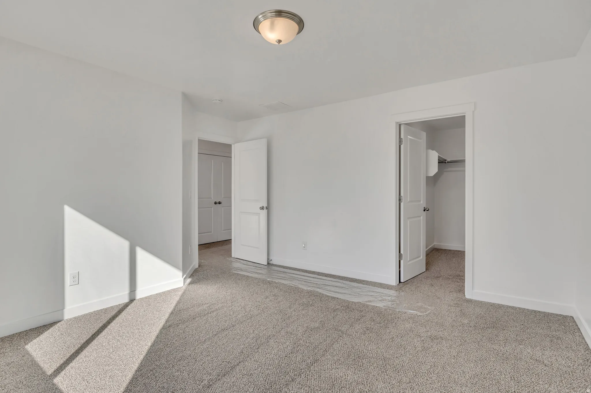 Unfurnished bedroom featuring a walk in closet and light colored carpet