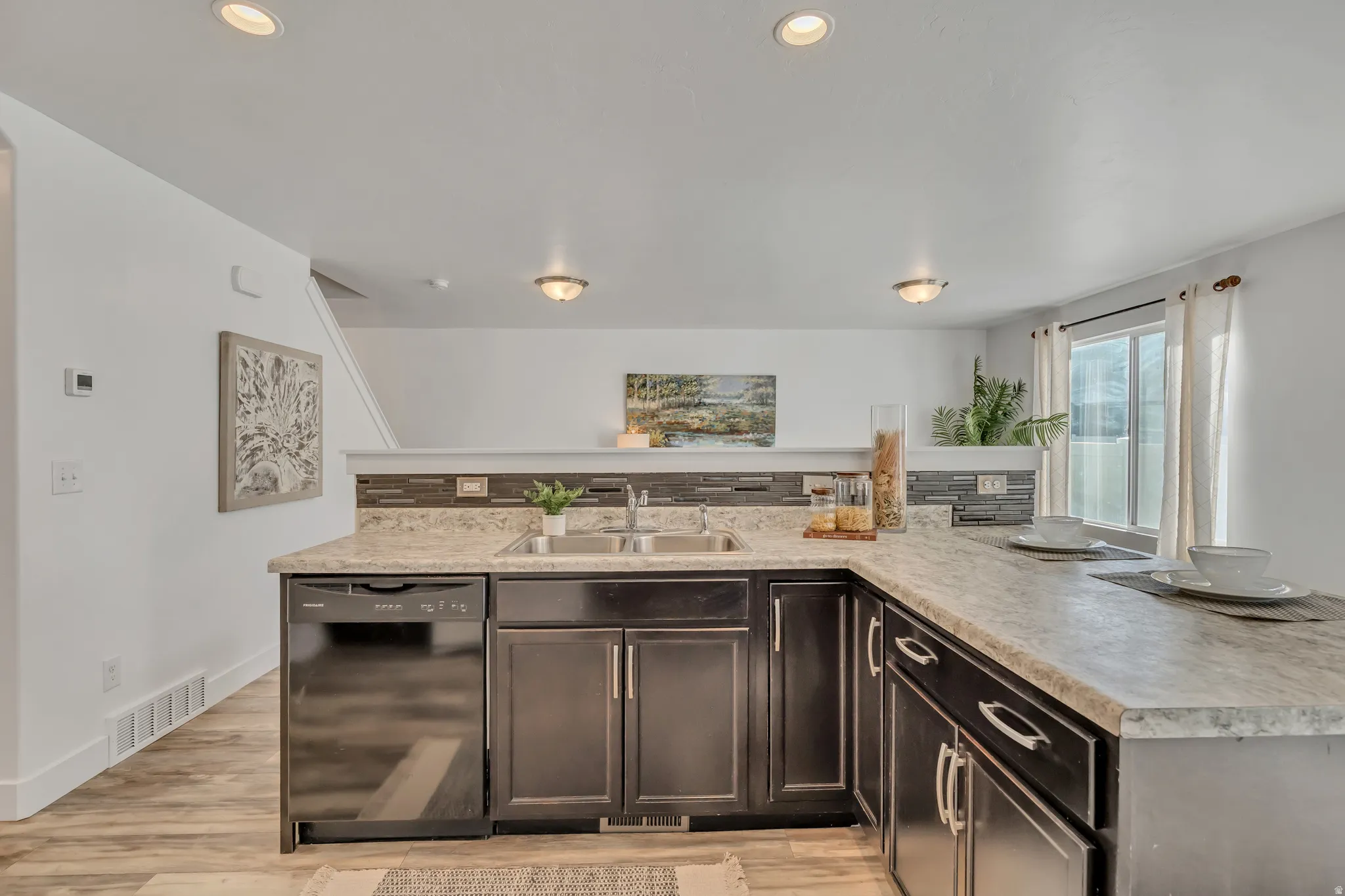 Kitchen featuring light countertops, dishwasher, dark wood finish cabinetry, light wood-style floors, and recessed lighting