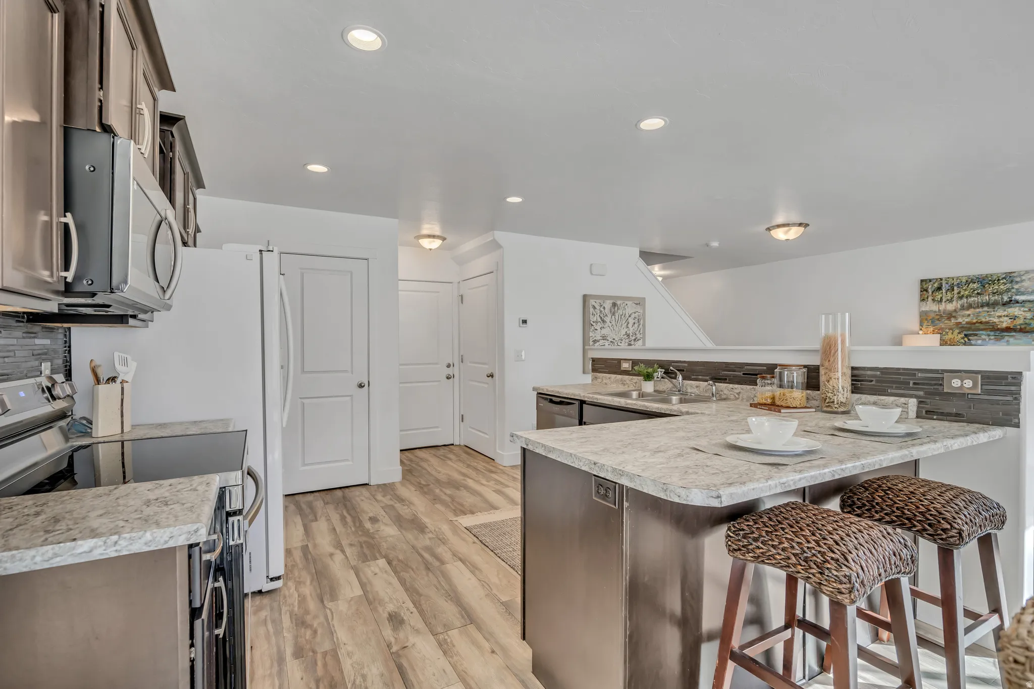 Kitchen with tasteful backsplash, stainless steel appliances, light countertops, a kitchen bar, and light wood-type flooring