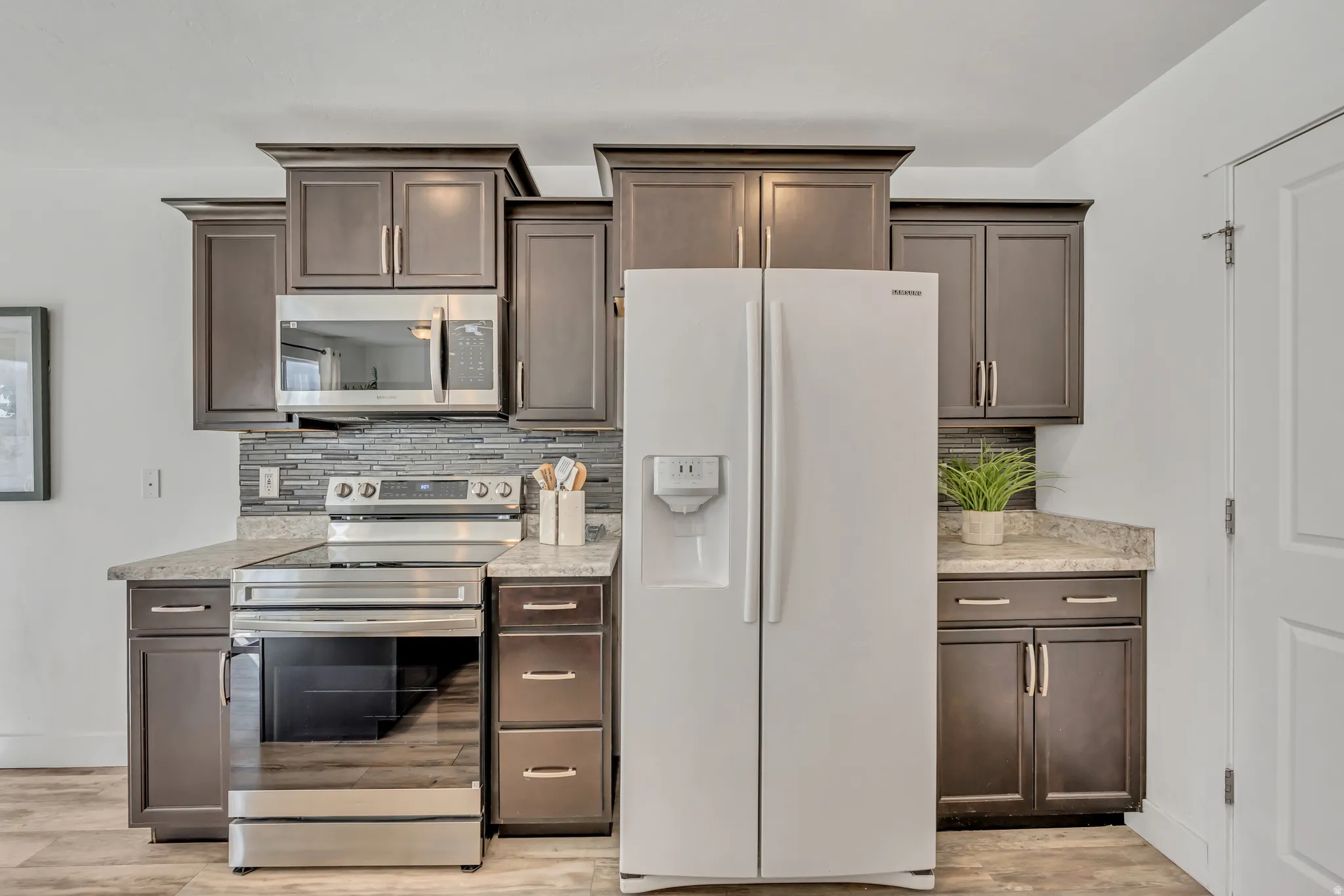 Kitchen featuring dark wood finish cabinets, stainless steel appliances, backsplash, and light wood-type flooring