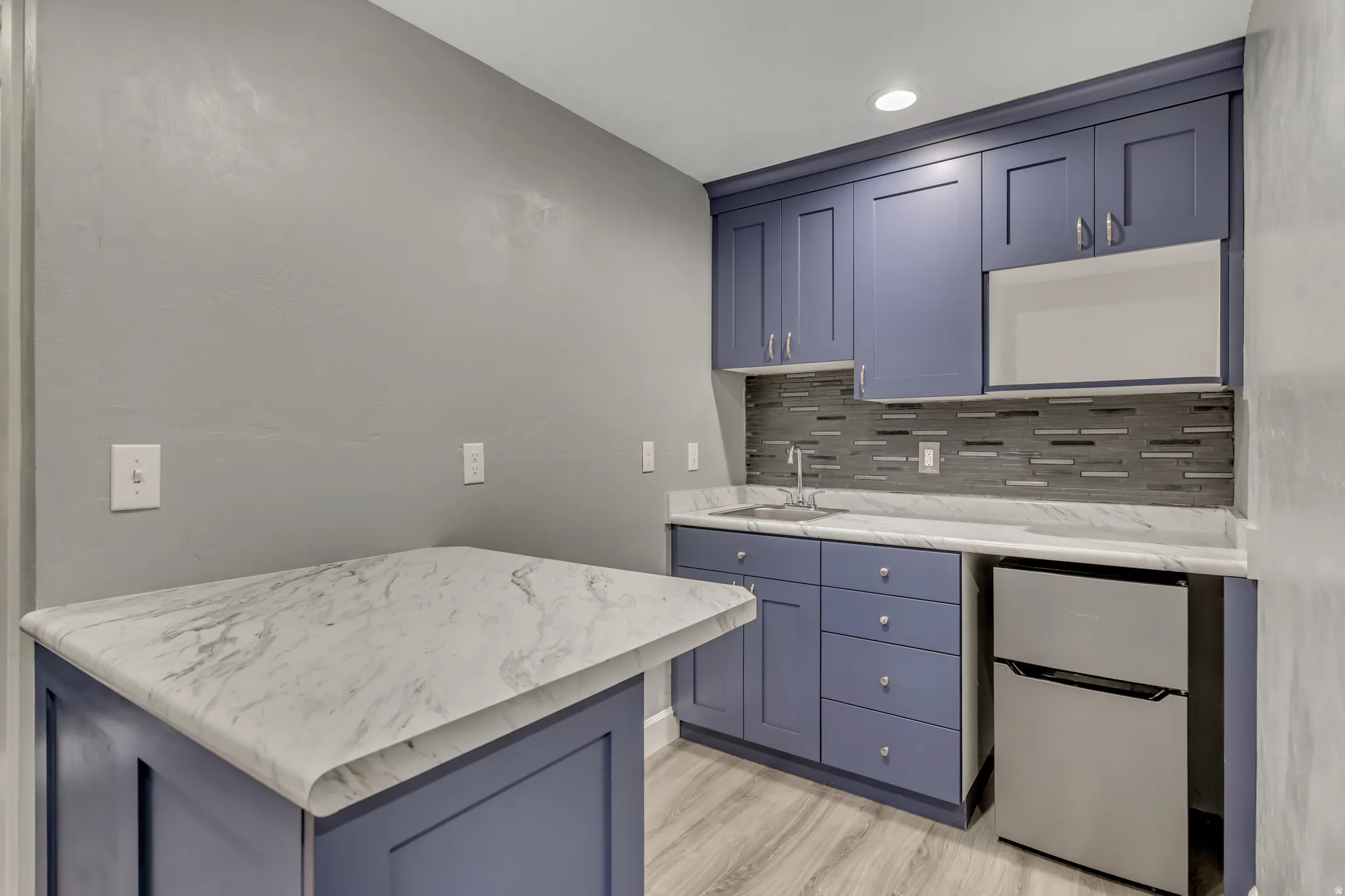 Bar area featuring blue cabinetry, freestanding refrigerator, light wood-style floors, tasteful backsplash, and recessed lighting