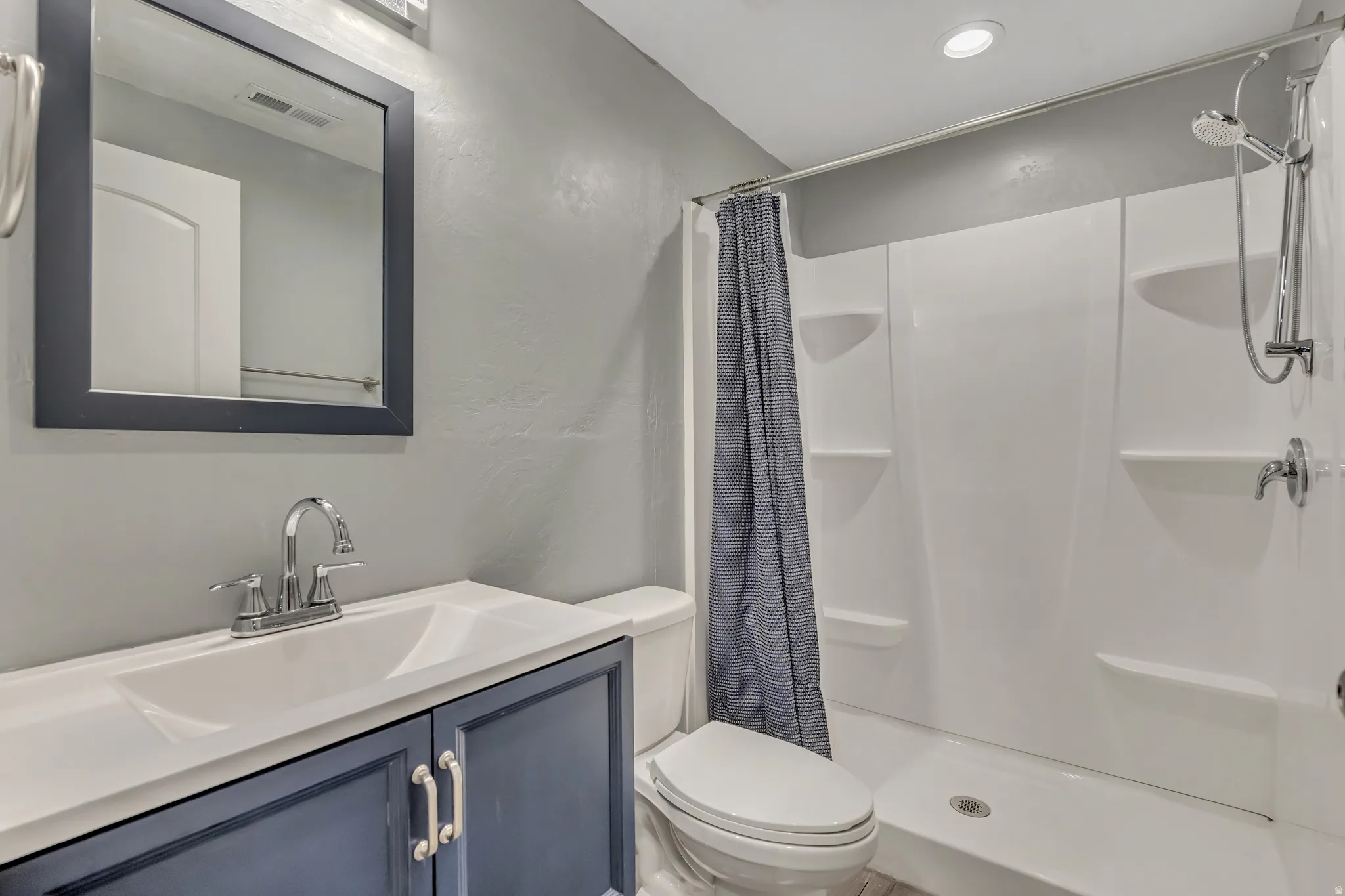 Bathroom featuring vanity, a shower stall, a textured wall, and recessed lighting