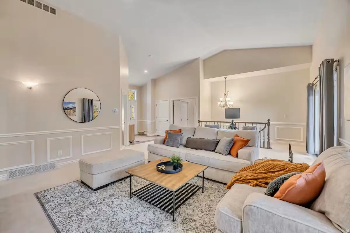 Living area featuring a decorative wall, a wainscoted wall, a chandelier, and vaulted ceiling