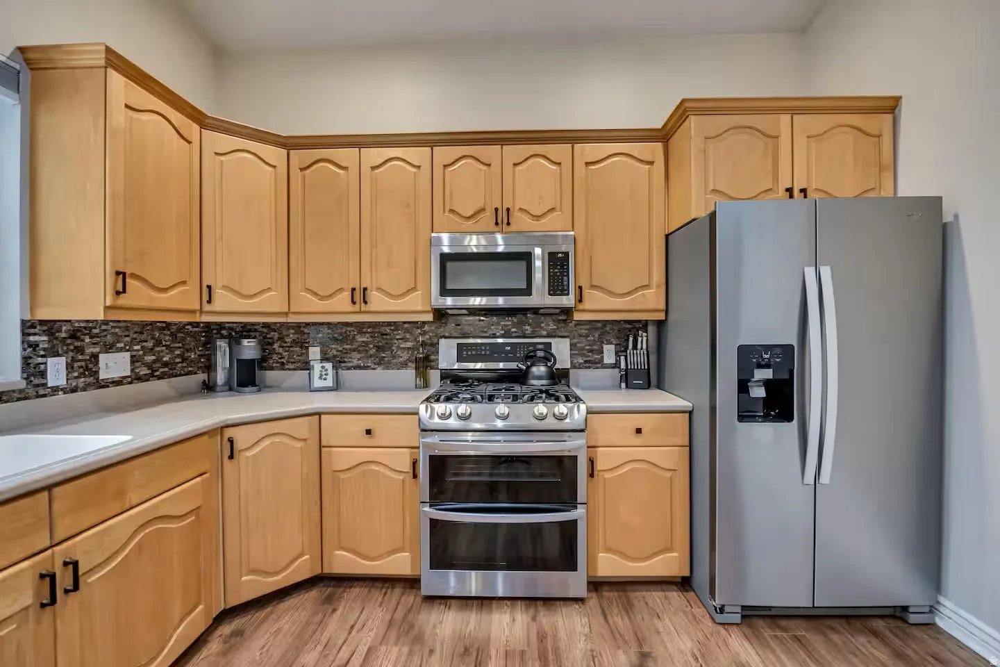 Kitchen with stainless steel appliances, light countertops, light wood finish cabinets, and light wood finished floors