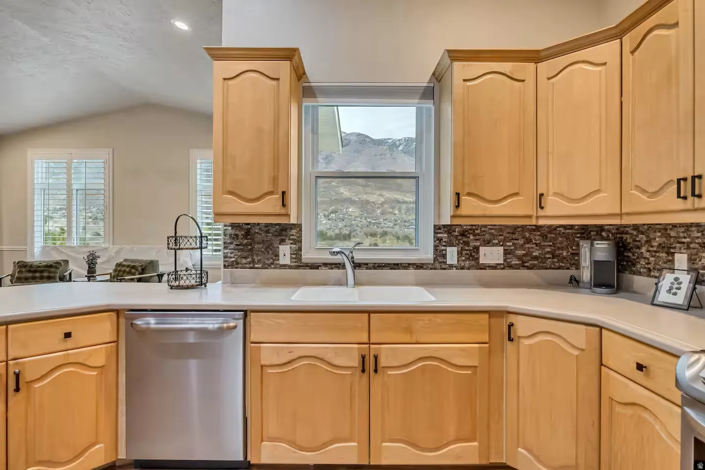 Kitchen with dishwasher, light wood finish cabinets, light countertops, backsplash, and lofted ceiling
