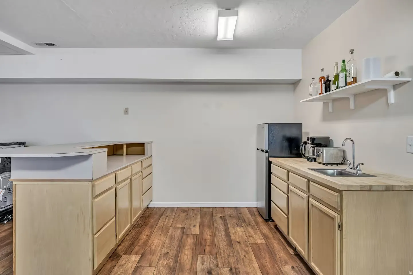 Kitchen featuring open shelves, light wood finish cabinetry, freestanding refrigerator, dark wood-style flooring, and a peninsula