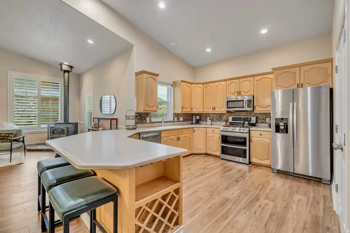 Kitchen with stainless steel appliances, a peninsula, light wood finish cabinetry, lofted ceiling, and light countertops