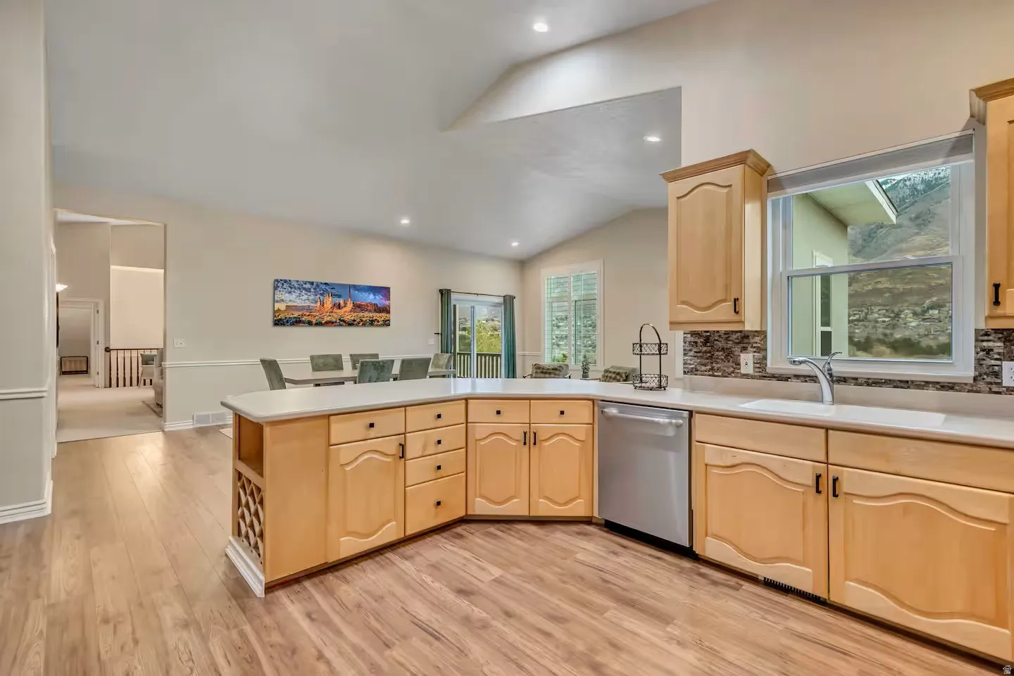 Kitchen with a peninsula, light wood finish cabinetry, decorative backsplash, light countertops, and dishwasher