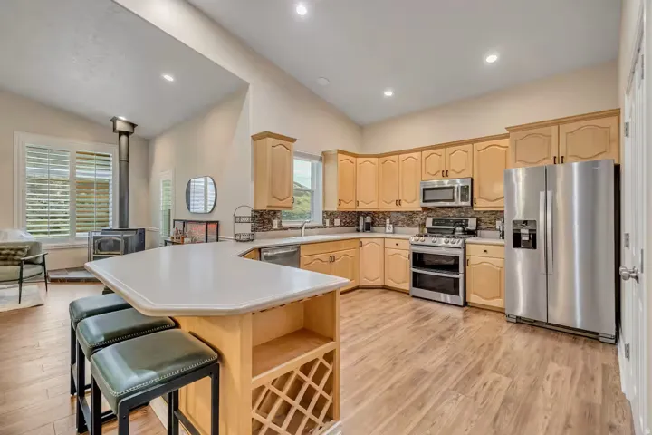 Kitchen with stainless steel appliances, a peninsula, light wood finish cabinetry, lofted ceiling, and light countertops