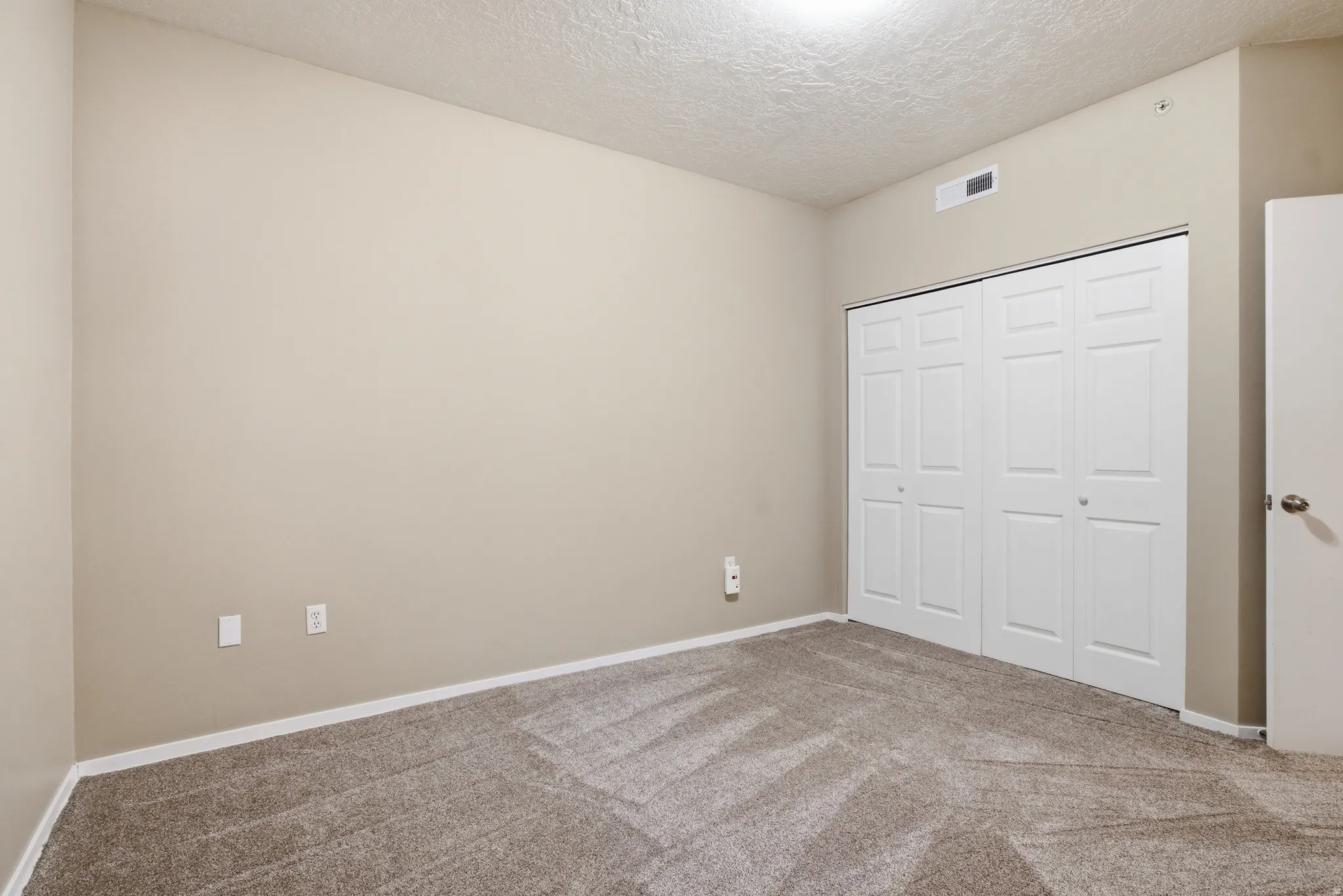 Unfurnished bedroom featuring closet, light colored carpet, and a textured ceiling