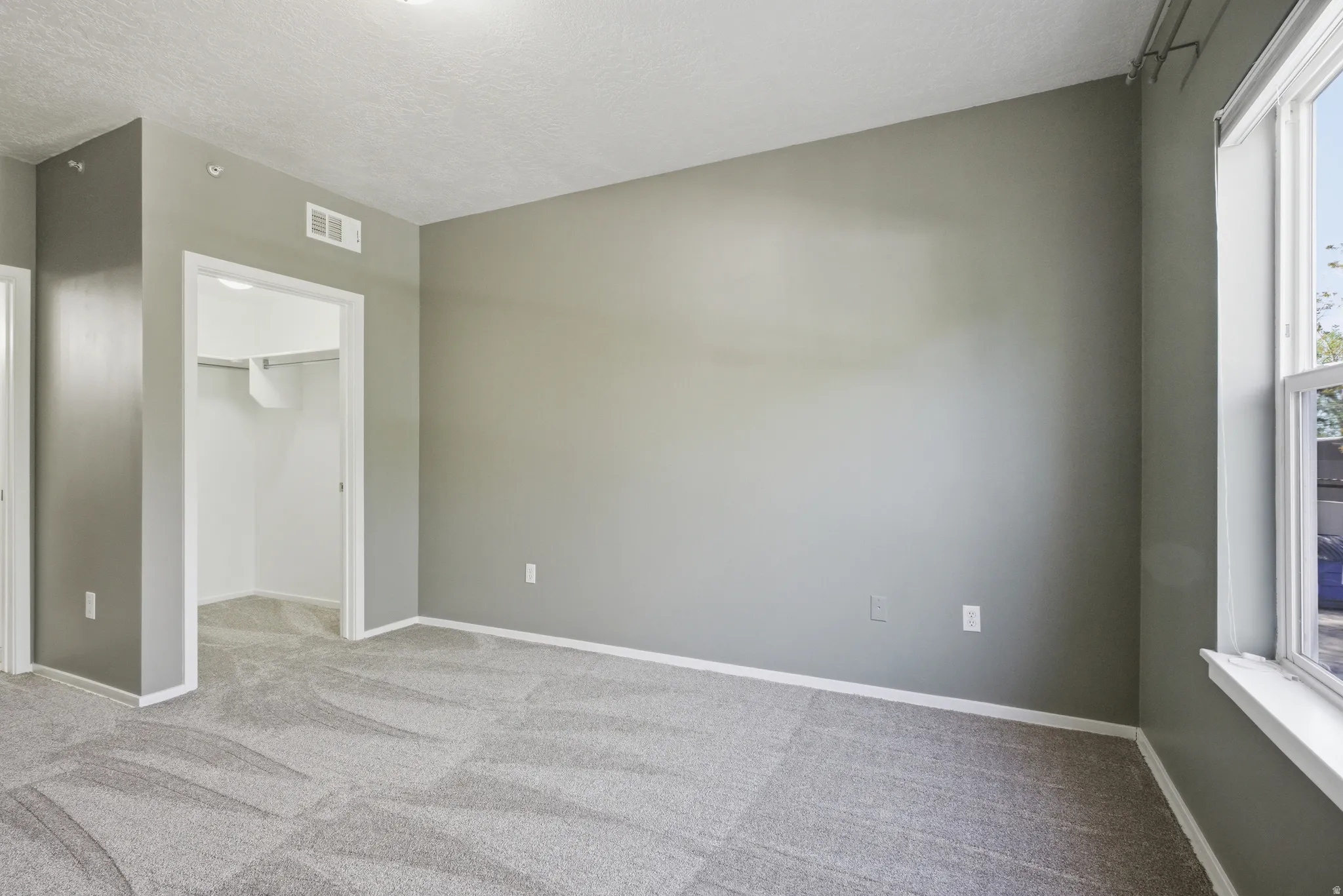 Unfurnished bedroom featuring a walk in closet, light colored carpet, and a textured ceiling