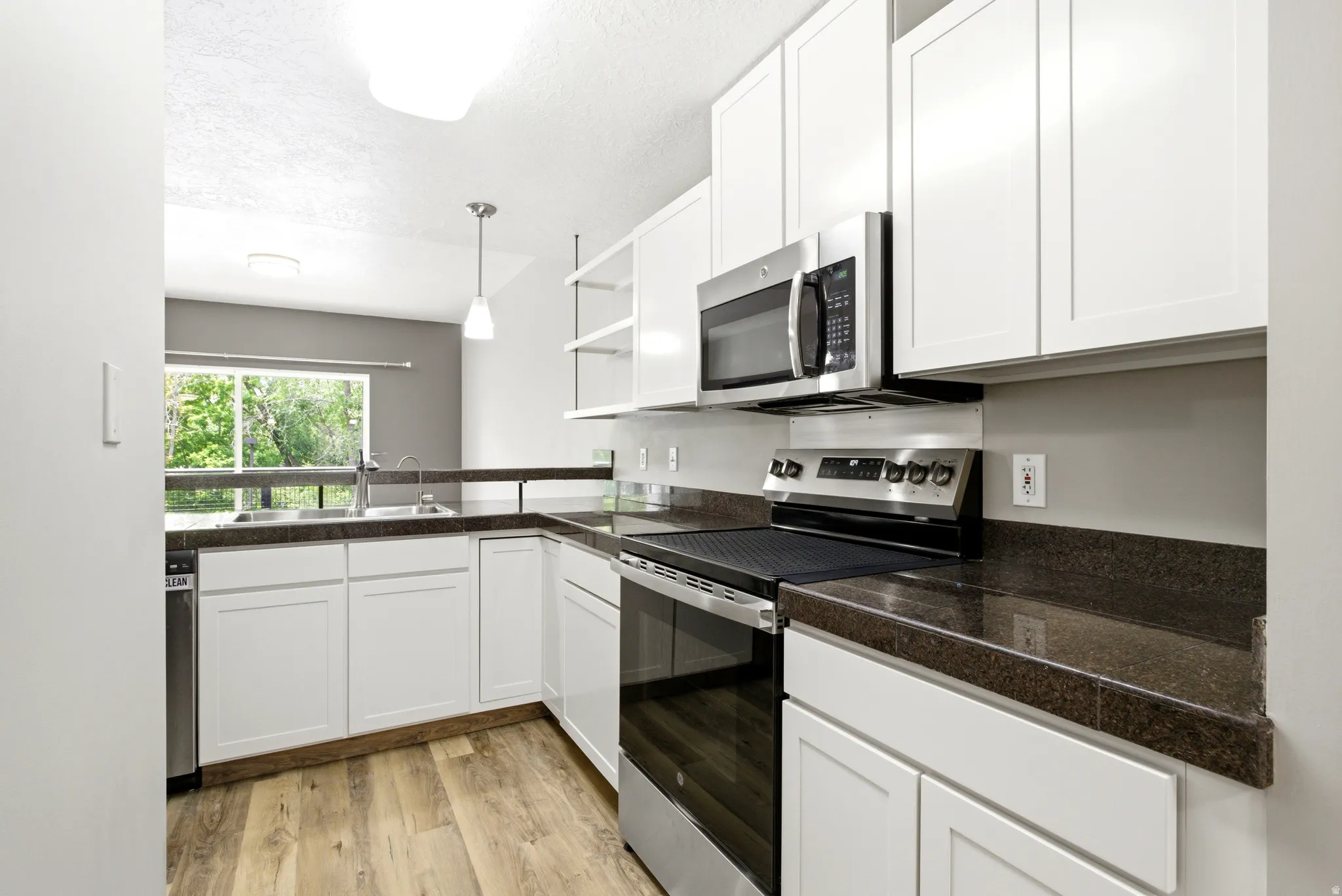 Kitchen featuring white shaker-style cabinetry, dark granite-finish countertops, stainless steel appliances including a built-in microwave and range, and wood-finish flooring