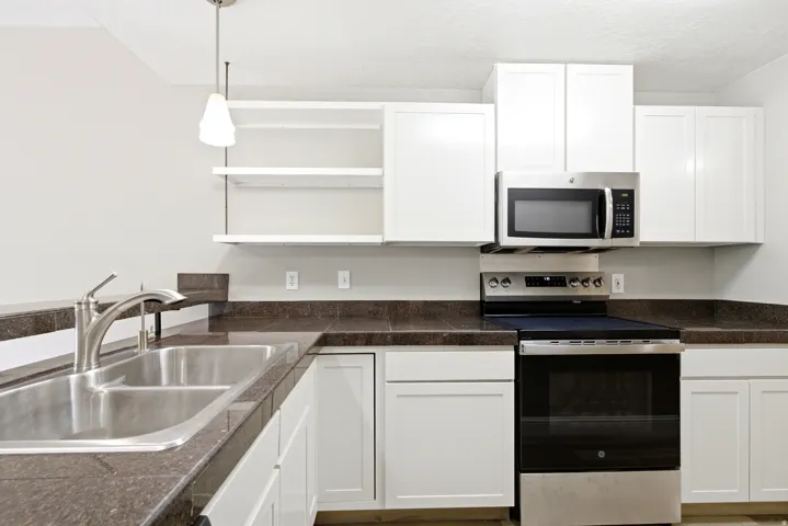 Kitchen featuring white cabinetry with brushed nickel hardware, dark stone-finish countertops, stainless steel double basin sink with brushed nickel faucet, stainless steel overhead microwave, and stainless steel range with a black cooktop