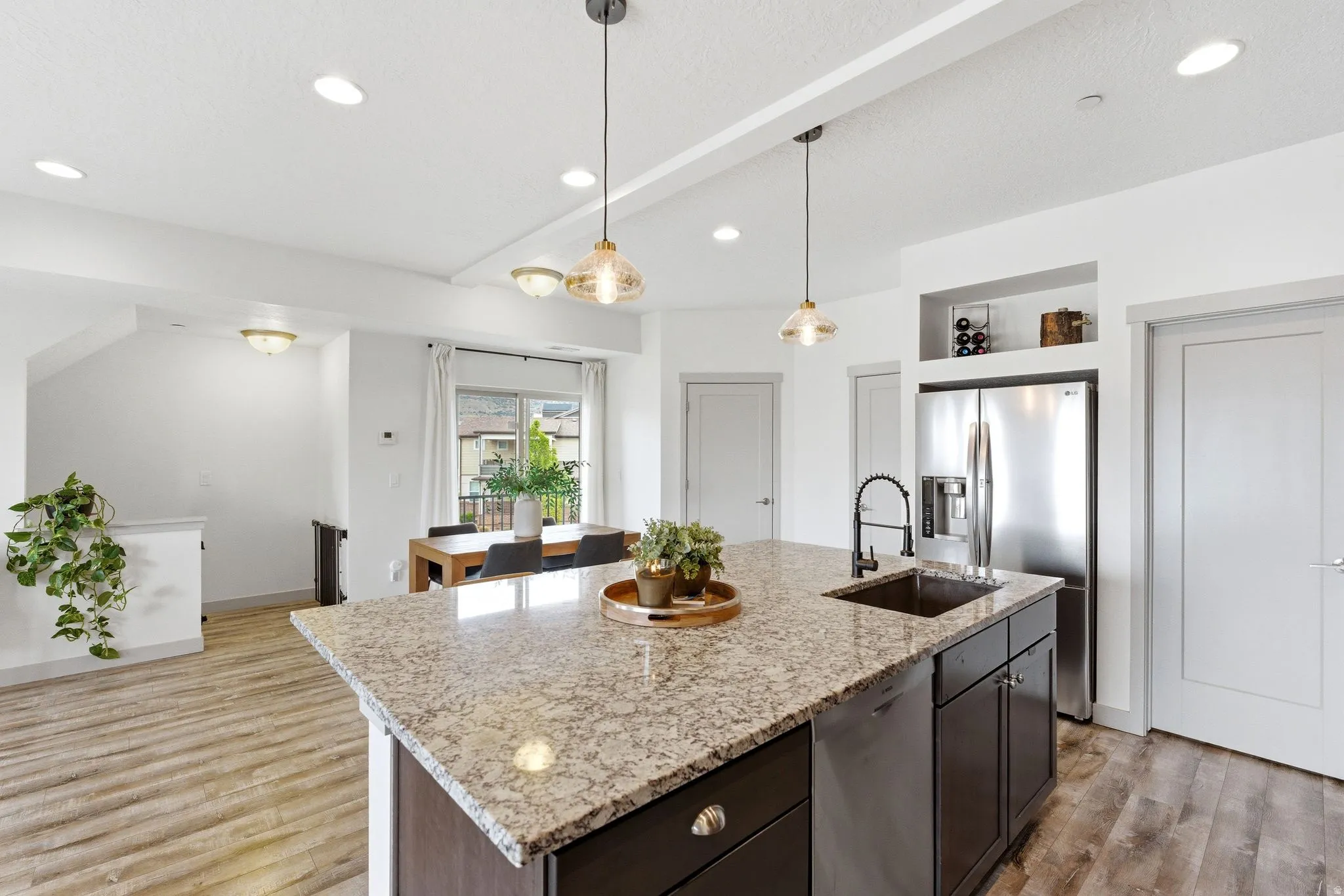 Kitchen with a kitchen island with sink, light stone countertops, stainless steel appliances, pendant lighting, and light wood-style floors