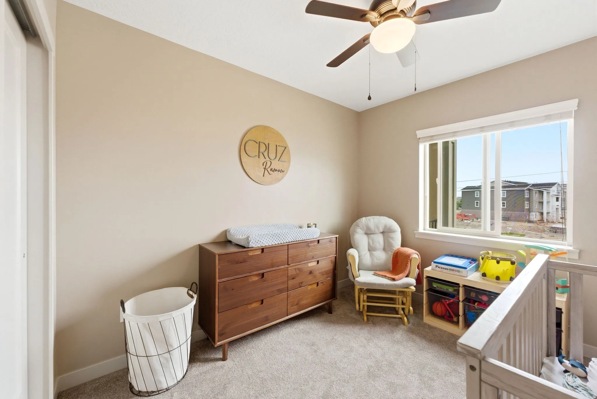 Bedroom featuring light colored carpet, a nursery area, and a ceiling fan