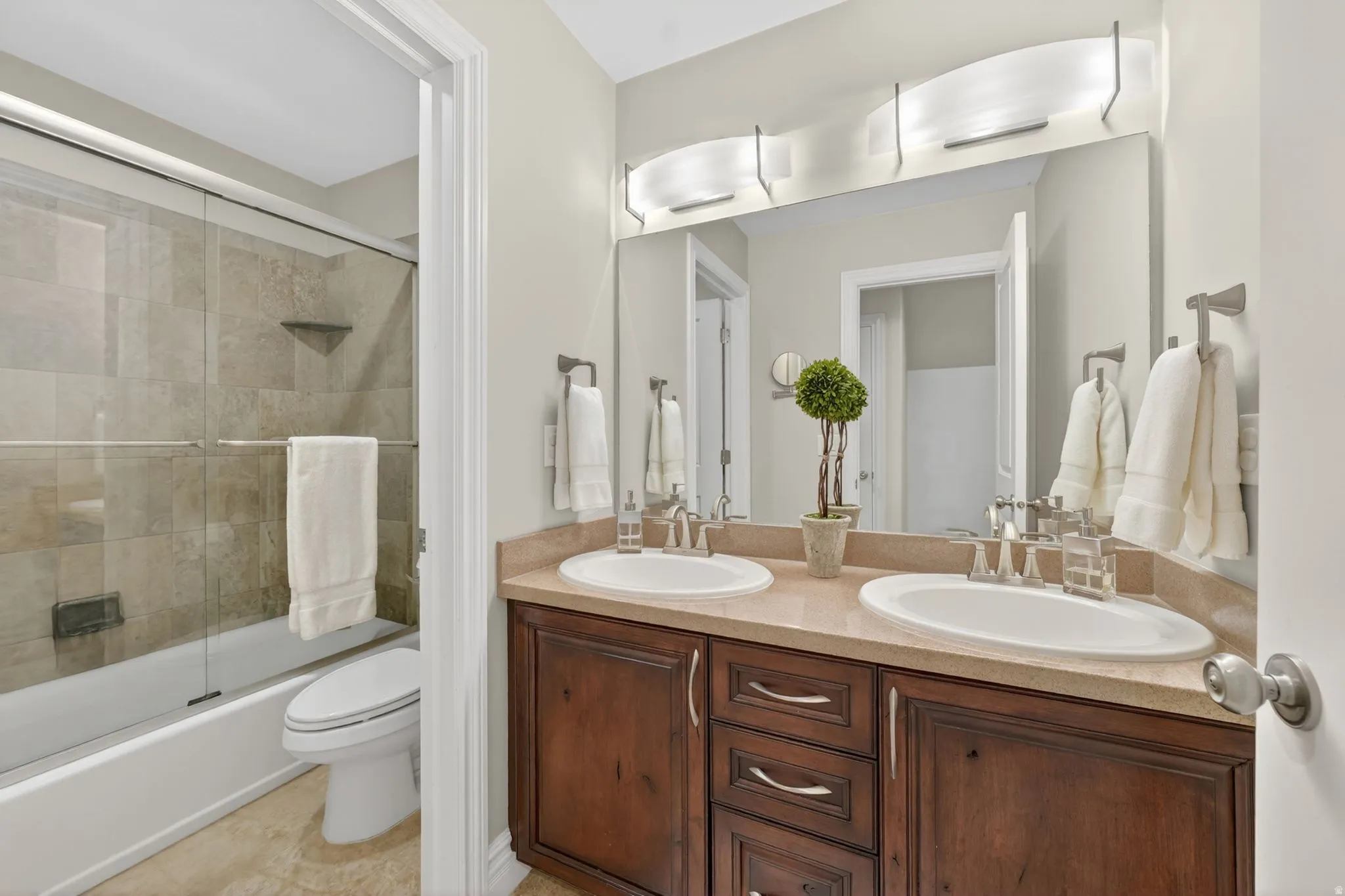 Full bath with double vanity and combined bath / shower with glass door