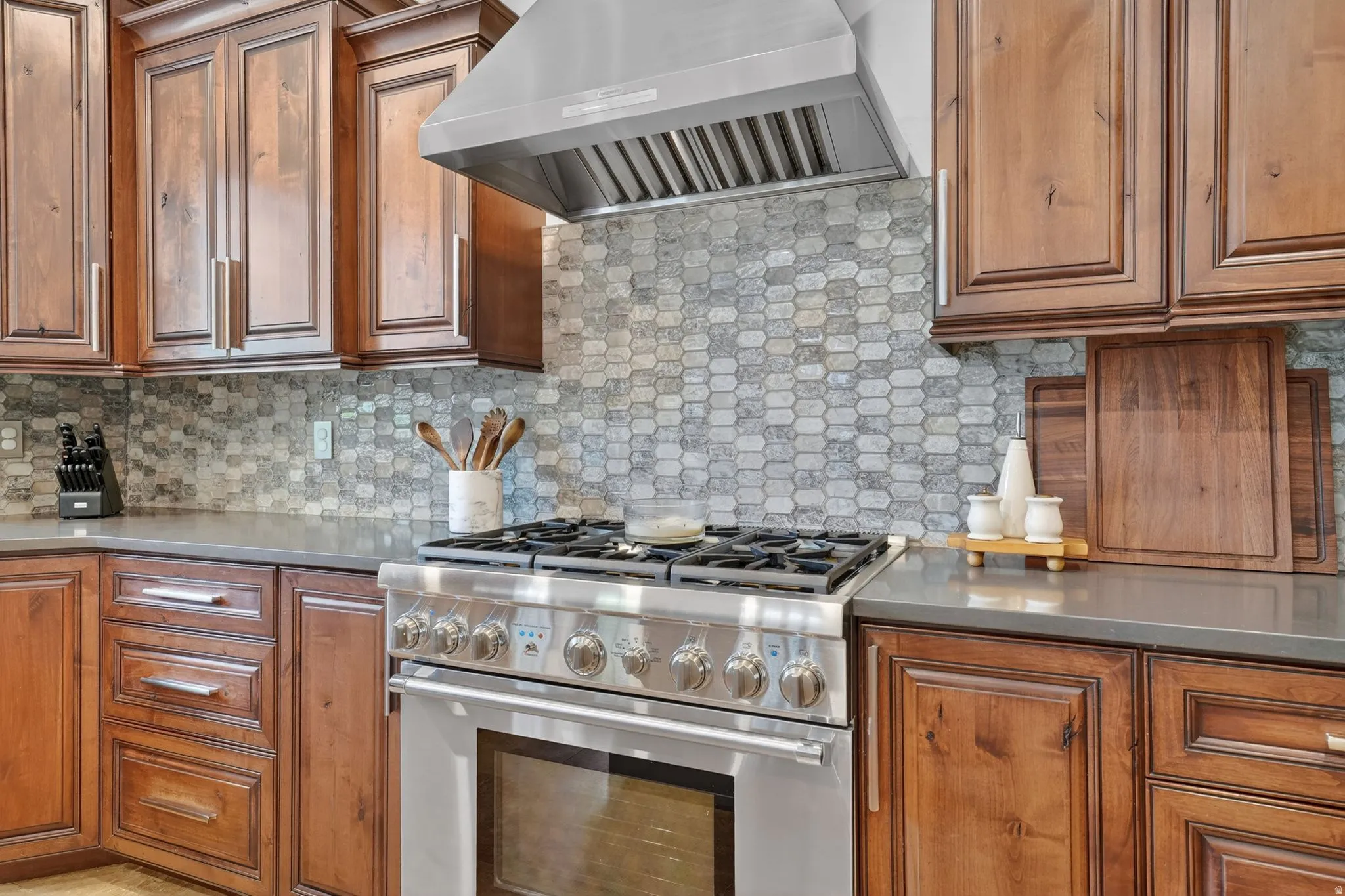Kitchen with high end stove, wood finish cabinets, decorative backsplash, and light stone counters