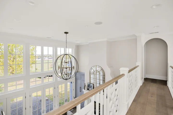 Hall with ornamental molding, hanging lights, hardwood / wood-style flooring, and an upstairs landing