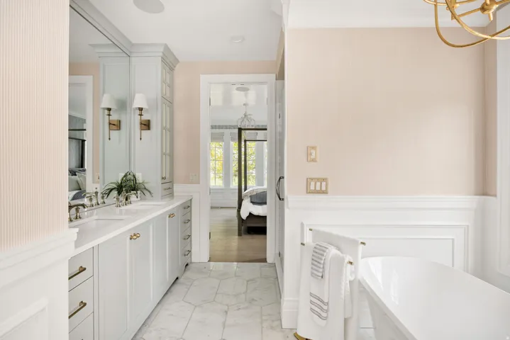 Ensuite bathroom with double vanity, a wainscoted wall, hanging lights, a soaking tub, and a decorative wall