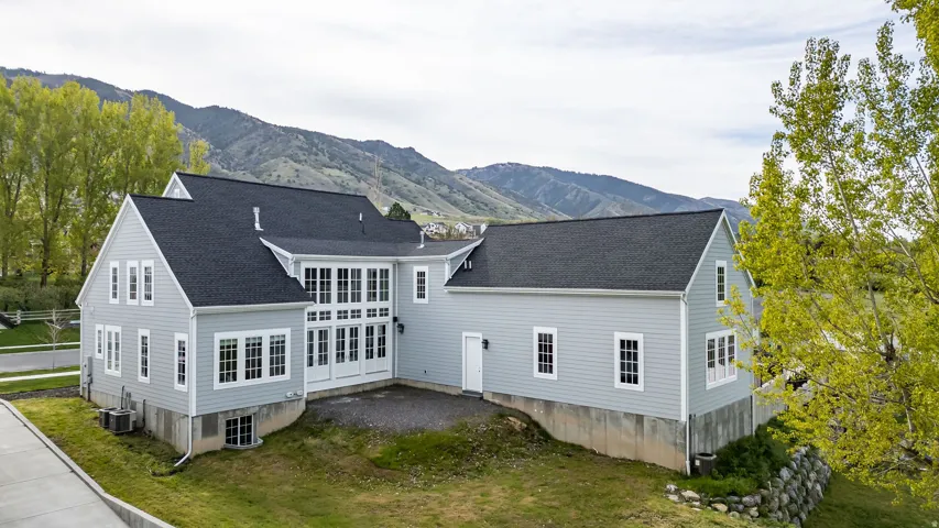 Back of house featuring a mountain view, a lawn, and roof with shingles