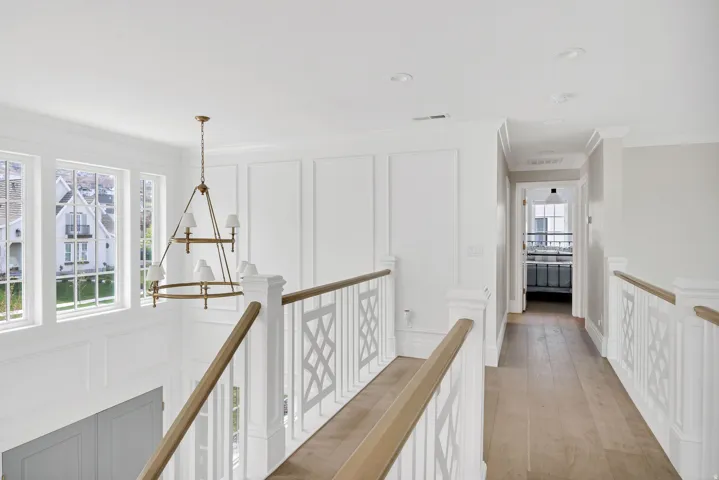 Hall featuring a decorative wall, suspended lighting, light wood-style floors, ornamental molding, and an upstairs landing
