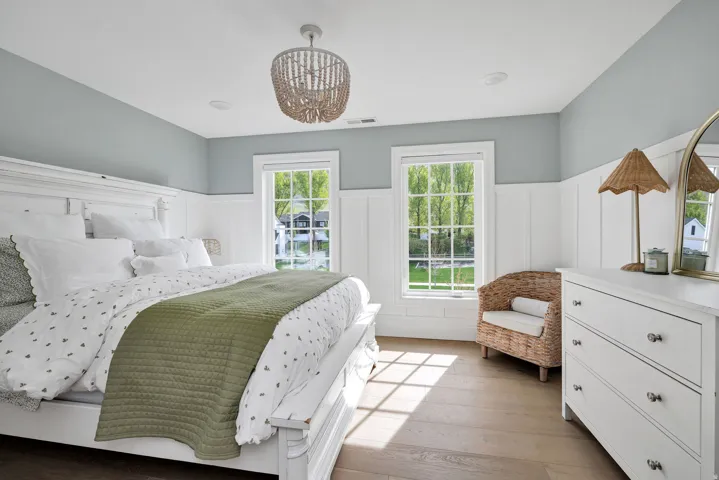 Bedroom with a decorative wall, light wood-style floors, hanging lights, and a wainscoted wall