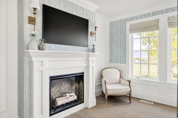 Living area featuring crown molding, wainscoting, light wood finished floors, a glass covered fireplace, and a decorative wall