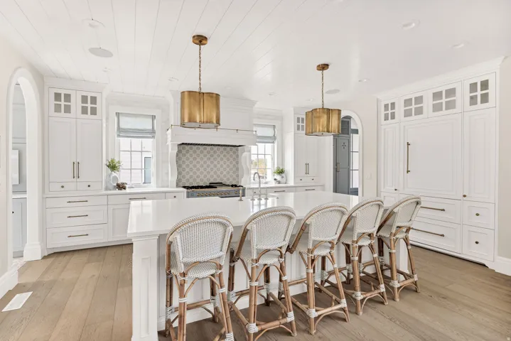 Kitchen featuring glass fronted cabinets, arched walkways, hanging light fixtures, an island with sink, and light wood-style floors