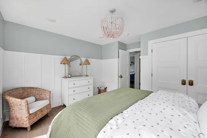 Bedroom featuring a decorative wall, hanging lights, a closet, a wainscoted wall, and wood finished floors
