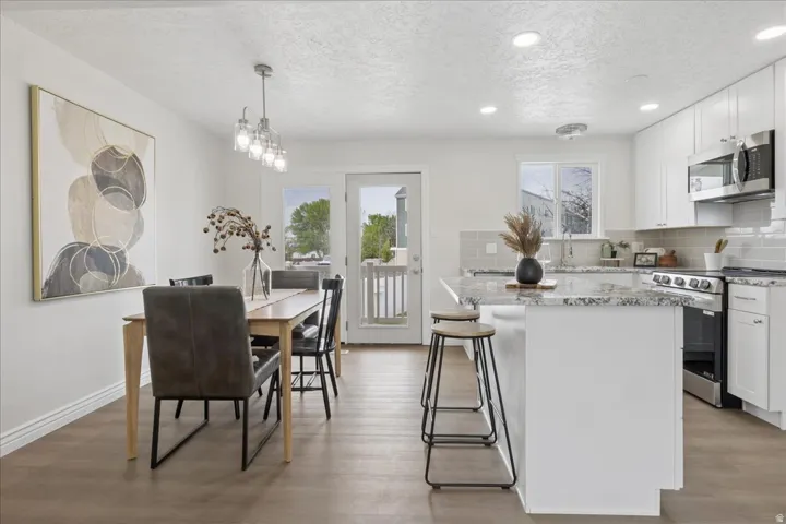 Kitchen with stainless steel appliances, decorative backsplash, white cabinetry, light stone counters, and light wood-style floors
