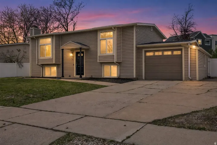 Split foyer home with concrete driveway, a chimney, an attached garage, and a front lawn