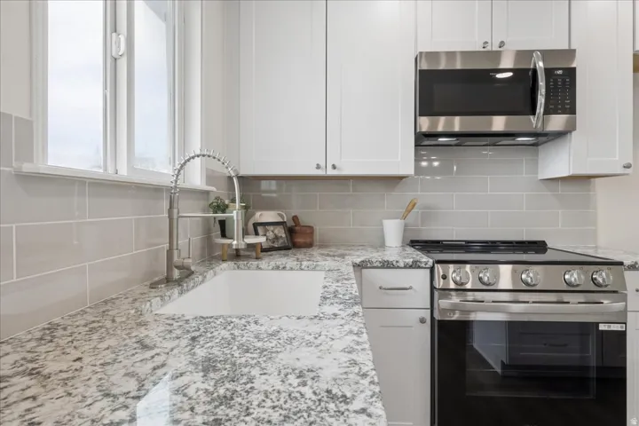 Kitchen with stainless steel appliances, white cabinetry, and light stone counters