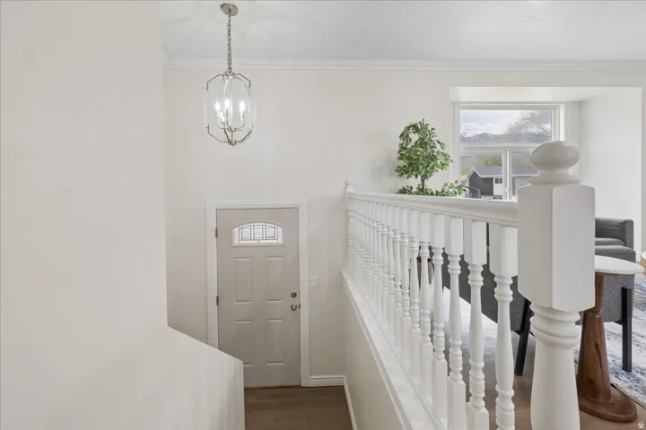 Foyer entrance featuring dark wood-style flooring, hanging lights, and ornamental molding