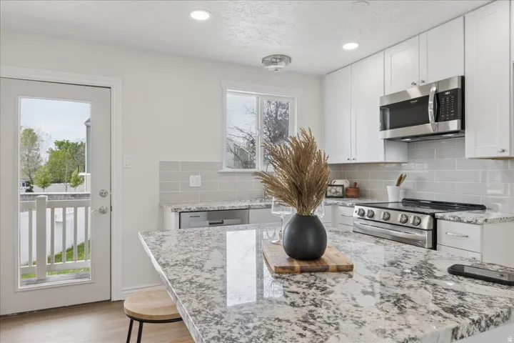 Kitchen with white cabinets, light stone counters, stainless steel appliances, recessed lighting, and backsplash
