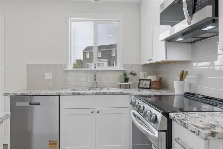 Kitchen with stainless steel appliances, white cabinetry, light stone countertops, and tasteful backsplash