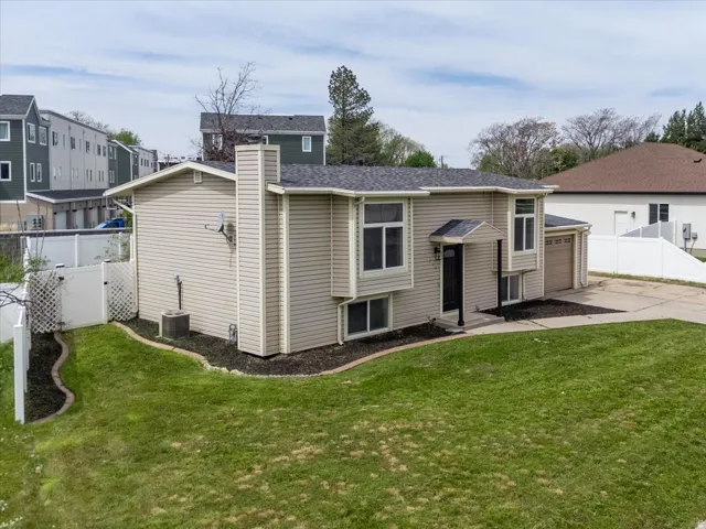 Rear view of property with a chimney, a garage, concrete driveway, and a shingled roof