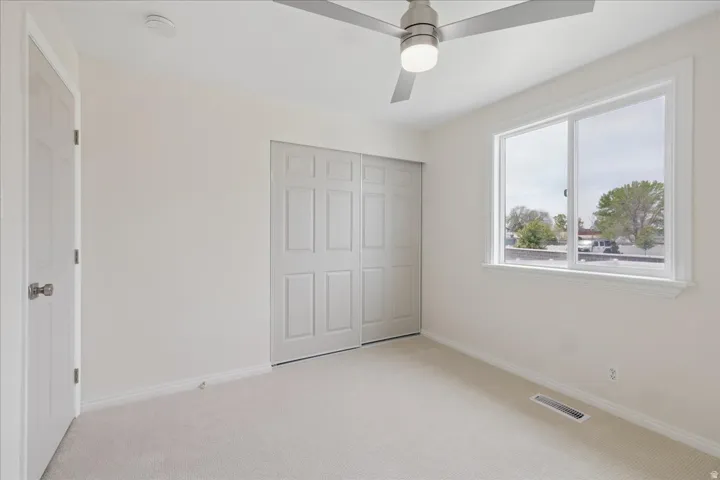 Unfurnished bedroom featuring light colored carpet, a closet, and a ceiling fan
