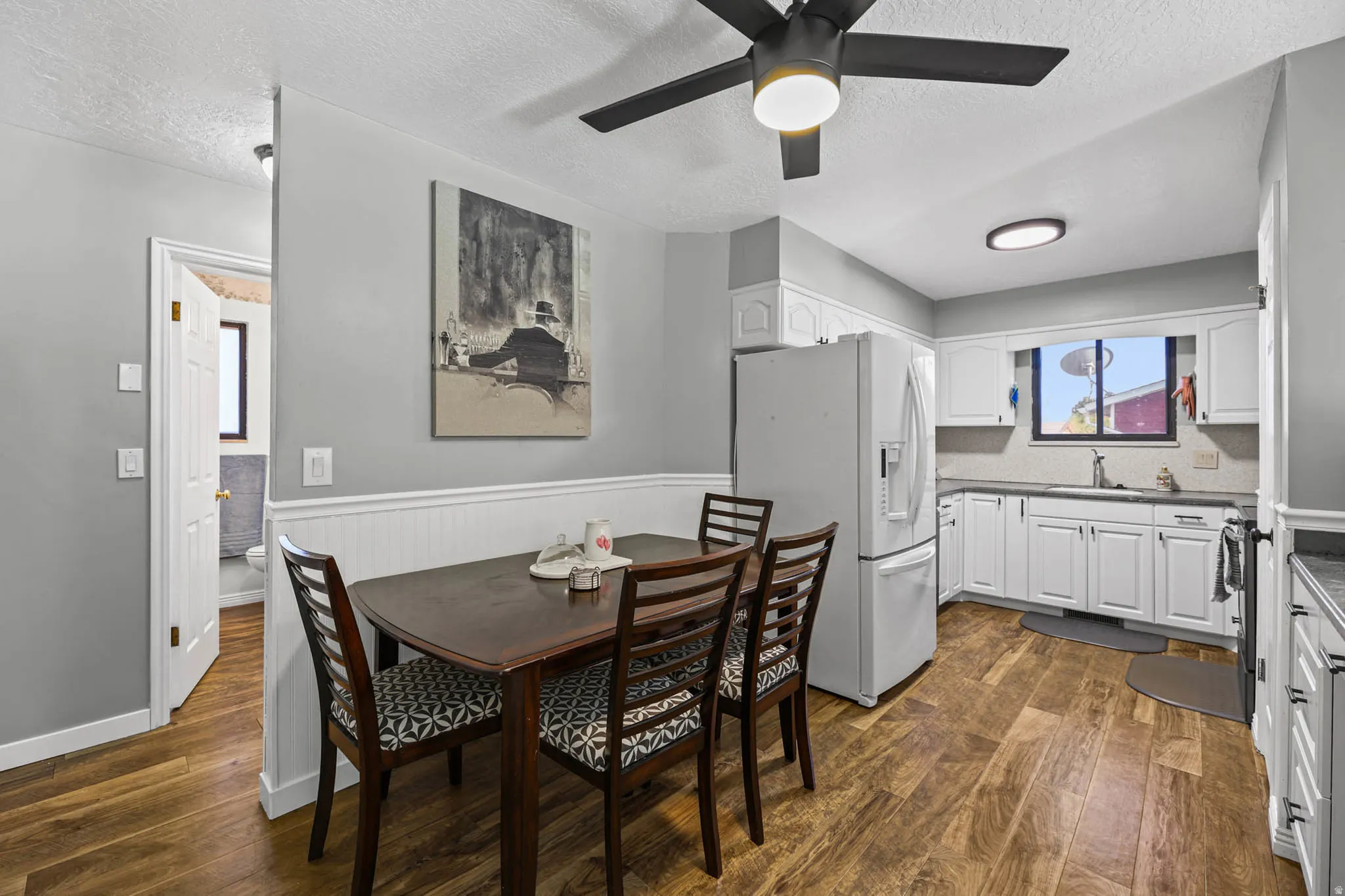 Dining space with a textured ceiling, a wainscoted wall, dark wood-type flooring, and a ceiling fan
