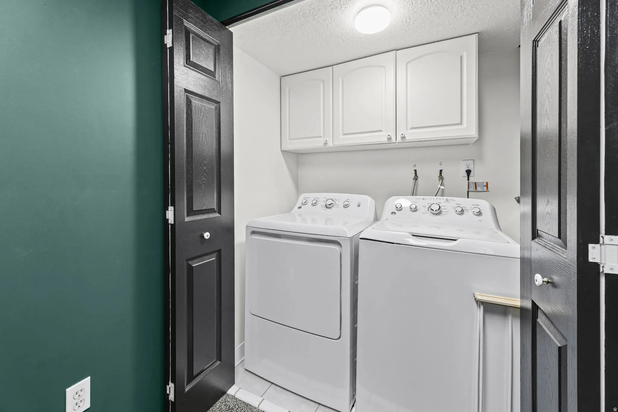 Laundry area with cabinet space, a textured ceiling, washer and dryer, and light tile patterned floors