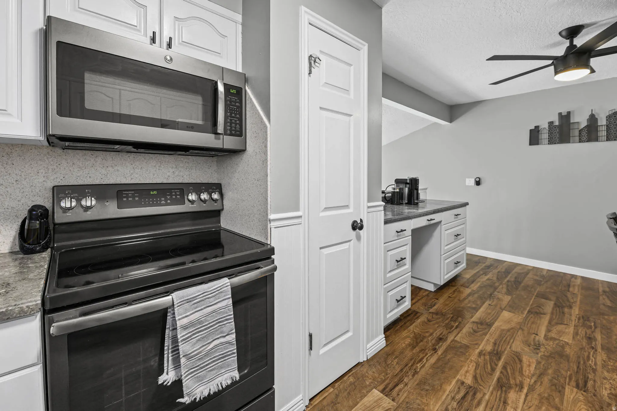 Kitchen featuring stainless steel appliances, white cabinetry, dark wood-style floors, built in desk, and a ceiling fan