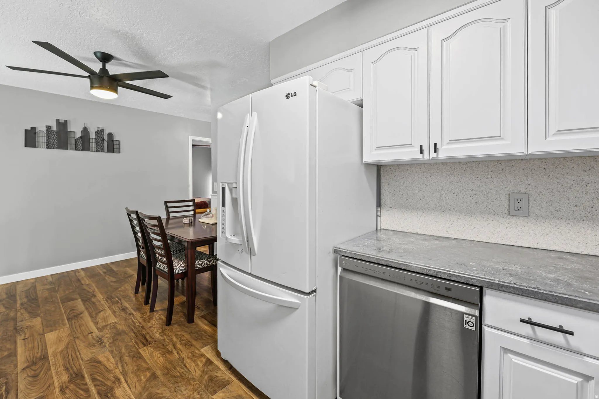 Kitchen with white cabinetry, stainless steel dishwasher, dark wood-style floors, ceiling fan, and a textured ceiling
