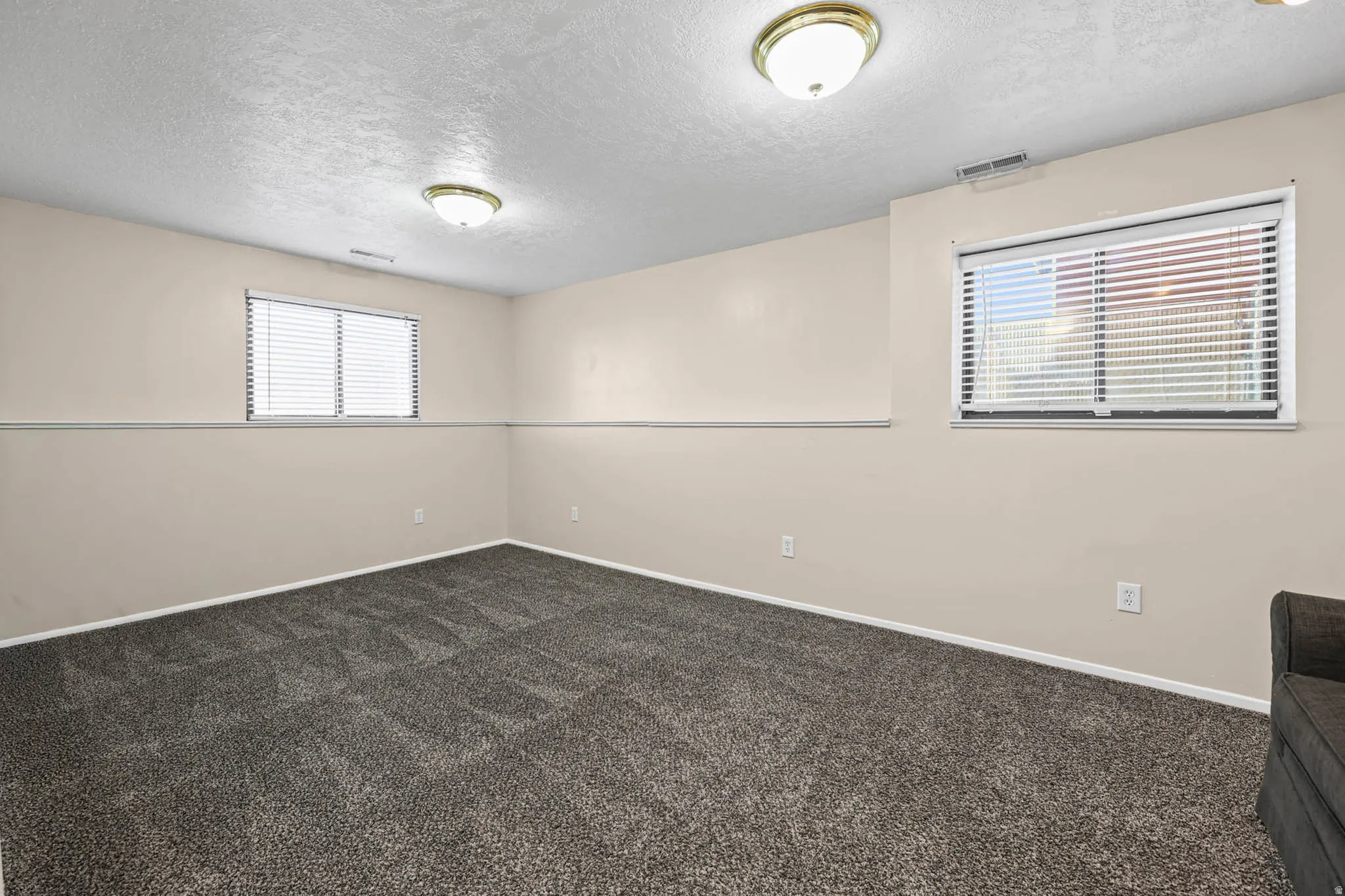 Spare room featuring dark colored carpet, a textured ceiling, and plenty of natural light